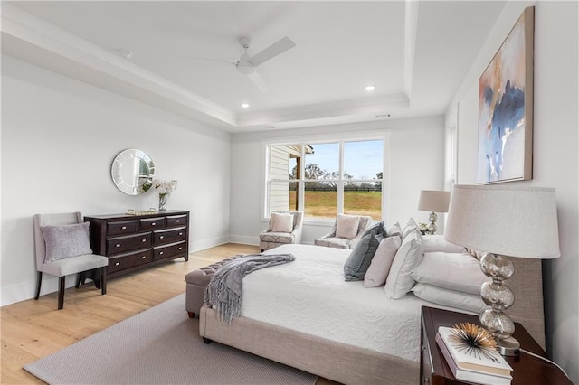 bedroom with a raised ceiling, ceiling fan, and light wood-type flooring