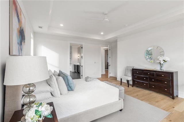 bedroom featuring ceiling fan, light hardwood / wood-style floors, a raised ceiling, and connected bathroom