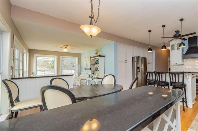 kitchen with pendant lighting, backsplash, white cabinetry, premium range hood, and stainless steel fridge with ice dispenser