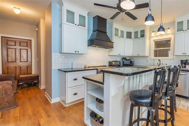 kitchen featuring dark countertops, hanging light fixtures, glass insert cabinets, white cabinetry, and premium range hood