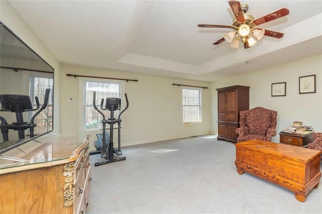 workout room featuring baseboards, a tray ceiling, ceiling fan, and light colored carpet