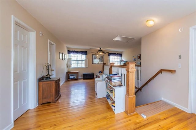 hallway featuring attic access, baseboards, light wood-style floors, and an upstairs landing