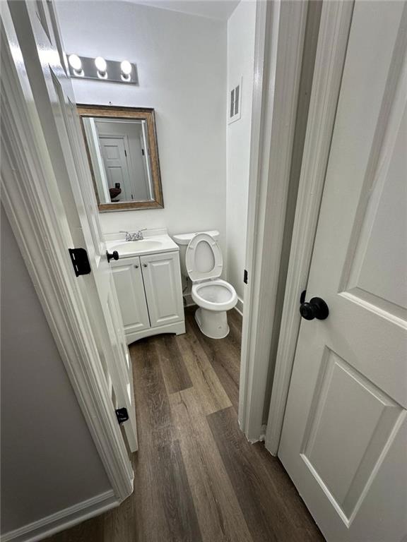 half bath with toilet, wood finished floors, and vanity