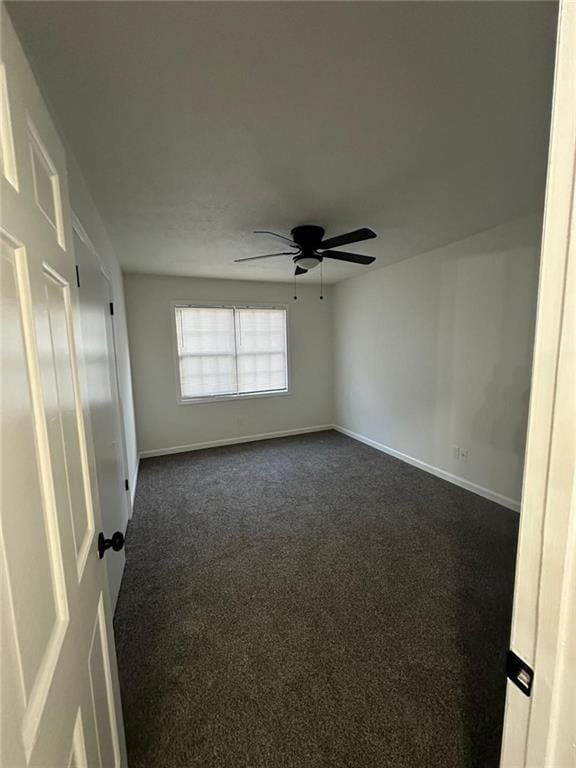 unfurnished room with dark colored carpet, a ceiling fan, and baseboards