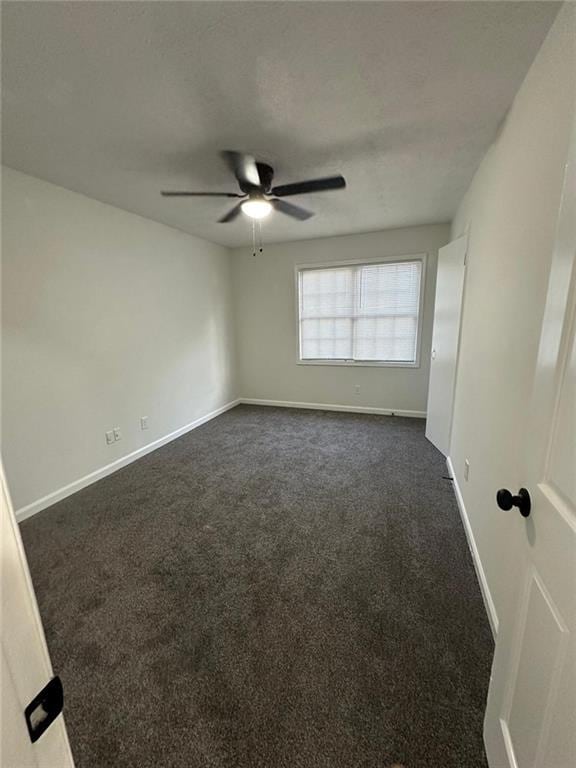 unfurnished room featuring a textured ceiling, dark colored carpet, a ceiling fan, and baseboards