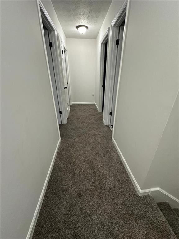 corridor featuring baseboards, dark carpet, and a textured ceiling