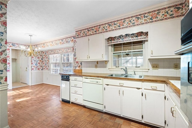 kitchen with sink, white dishwasher, pendant lighting, light parquet floors, and white cabinets