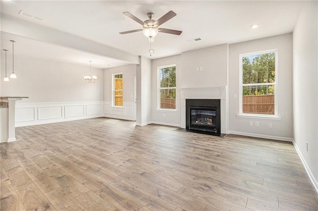 unfurnished living room featuring visible vents, a wealth of natural light, a fireplace with flush hearth, and ceiling fan with notable chandelier