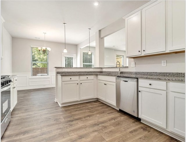 kitchen featuring light wood-type flooring, a peninsula, a wainscoted wall, white cabinets, and appliances with stainless steel finishes