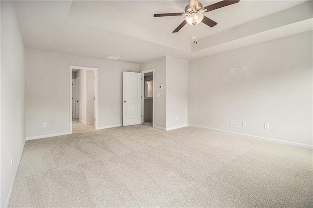 spare room featuring baseboards, a tray ceiling, light colored carpet, and a ceiling fan
