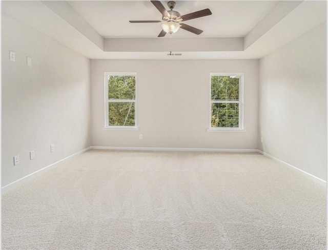 empty room with a wealth of natural light, ceiling fan, baseboards, and a raised ceiling