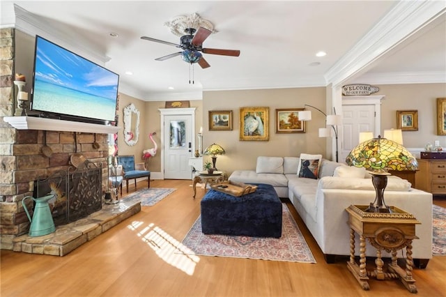 living room with ornamental molding, a stone fireplace, hardwood / wood-style floors, and ceiling fan