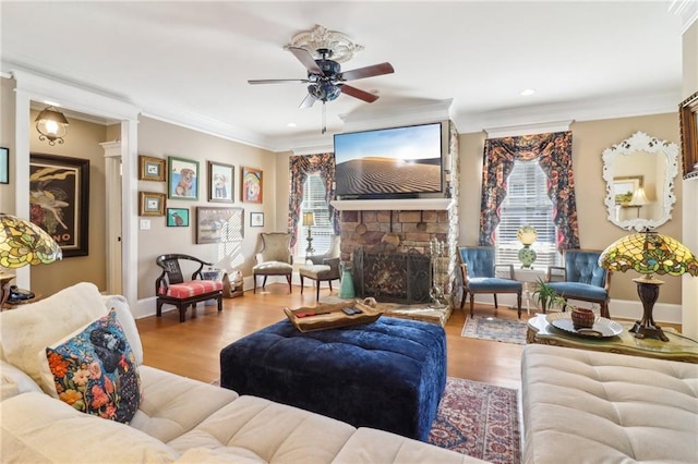 living room featuring crown molding, ceiling fan, wood-type flooring, and a stone fireplace