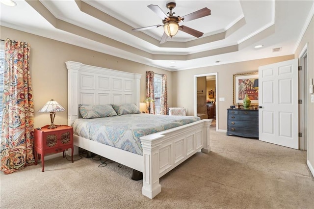 bedroom with connected bathroom, light carpet, ornamental molding, a raised ceiling, and ceiling fan