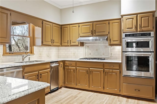 kitchen with appliances with stainless steel finishes, light stone countertops, crown molding, under cabinet range hood, and a sink