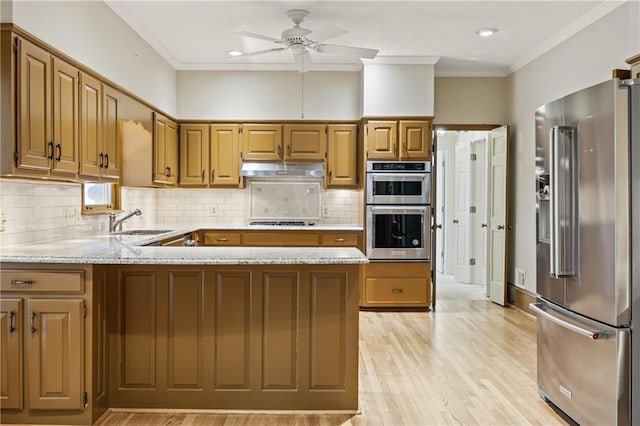 kitchen featuring light wood-style flooring, under cabinet range hood, stainless steel appliances, a peninsula, and a sink