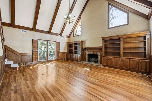 unfurnished living room featuring beam ceiling, wainscoting, a fireplace, and visible vents