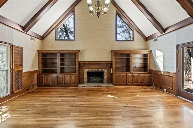 unfurnished living room with light wood-type flooring, beamed ceiling, wainscoting, and visible vents