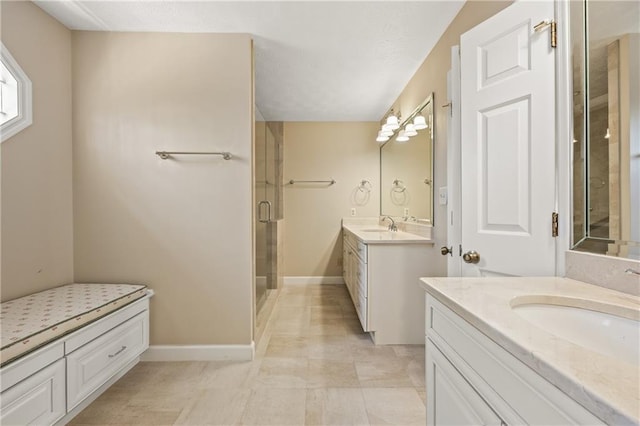 bathroom featuring a stall shower, two vanities, a sink, and baseboards