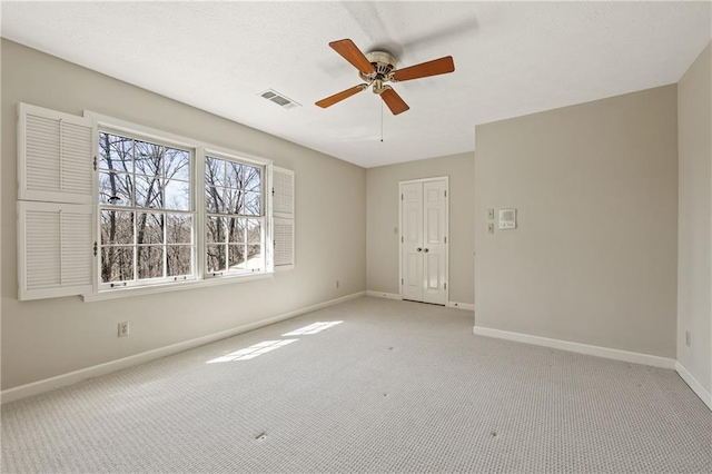 empty room with light carpet, visible vents, baseboards, and ceiling fan