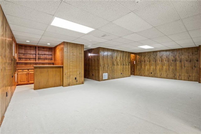 finished basement with wood walls, visible vents, and light colored carpet