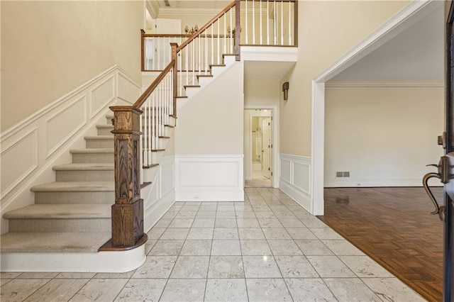 foyer entrance with crown molding, visible vents, a decorative wall, a towering ceiling, and stairs