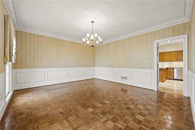 empty room with visible vents, ornamental molding, wainscoting, an inviting chandelier, and wallpapered walls