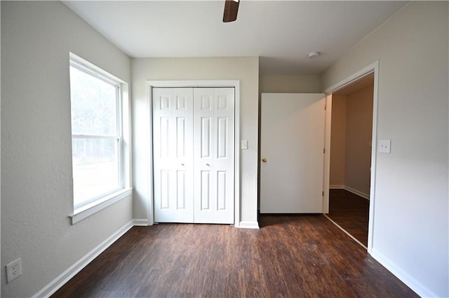 unfurnished bedroom featuring multiple windows, ceiling fan, a closet, and dark wood-type flooring