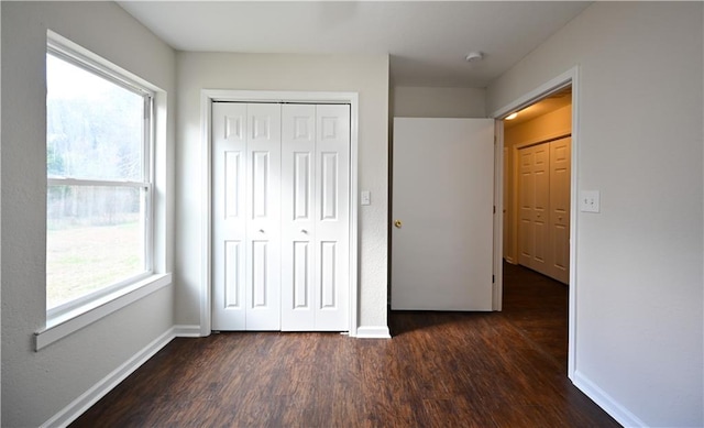 unfurnished bedroom with dark wood-style floors, a closet, and baseboards