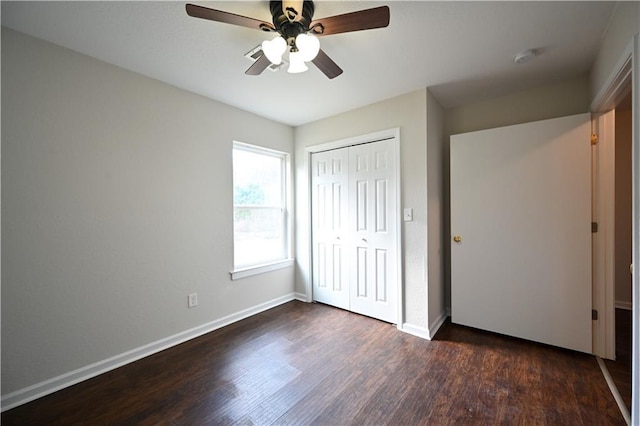 unfurnished bedroom with dark wood-type flooring, a closet, baseboards, and a ceiling fan