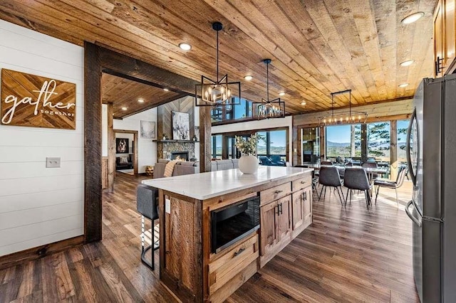 kitchen featuring decorative light fixtures, a center island, black microwave, wooden ceiling, and stainless steel fridge