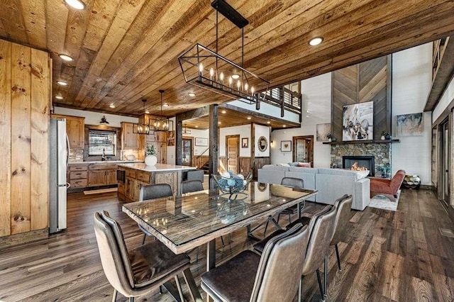 dining area with dark wood-type flooring, sink, wooden ceiling, a notable chandelier, and a fireplace