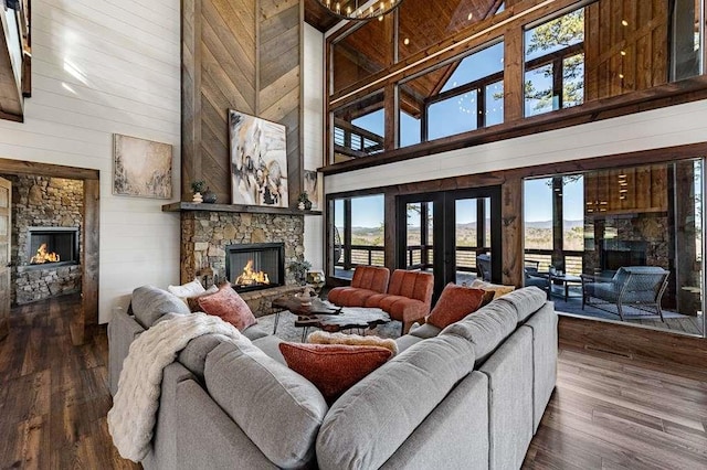 living room featuring french doors, a stone fireplace, dark hardwood / wood-style flooring, and wood walls