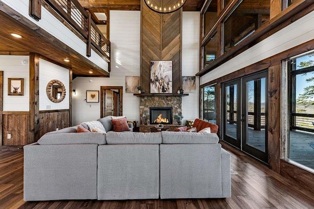 living room featuring a towering ceiling, dark hardwood / wood-style floors, a healthy amount of sunlight, and wood walls