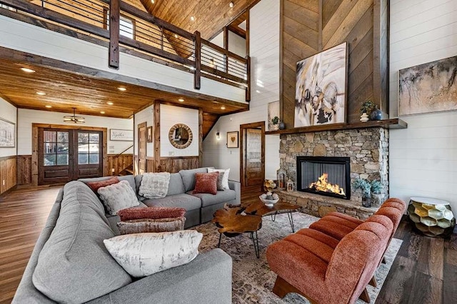 living room featuring a stone fireplace, wooden walls, hardwood / wood-style flooring, wooden ceiling, and french doors