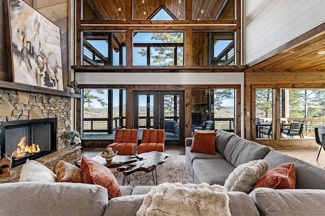 living room featuring wood-type flooring, a stone fireplace, plenty of natural light, and french doors