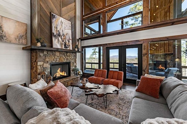 living room featuring a stone fireplace, wooden walls, french doors, and a high ceiling