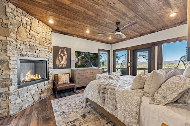 bedroom with a stone fireplace, dark hardwood / wood-style floors, access to exterior, ceiling fan, and wood ceiling