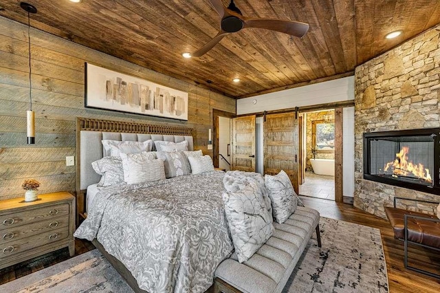 bedroom featuring wooden walls, a fireplace, dark hardwood / wood-style flooring, wood ceiling, and a barn door