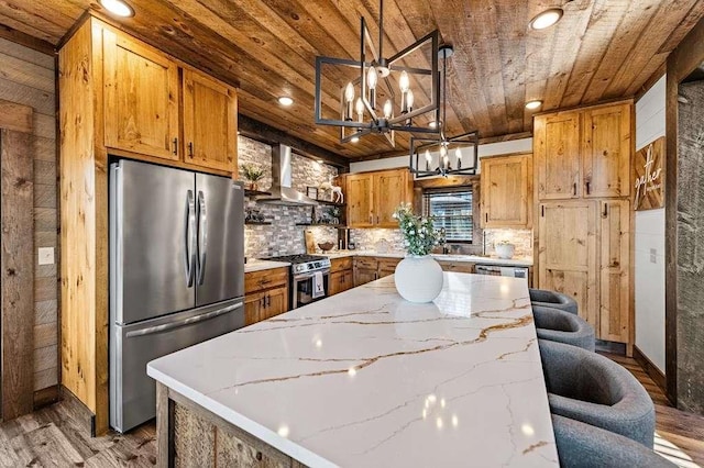 kitchen with hanging light fixtures, wood ceiling, stainless steel appliances, light stone countertops, and wall chimney exhaust hood