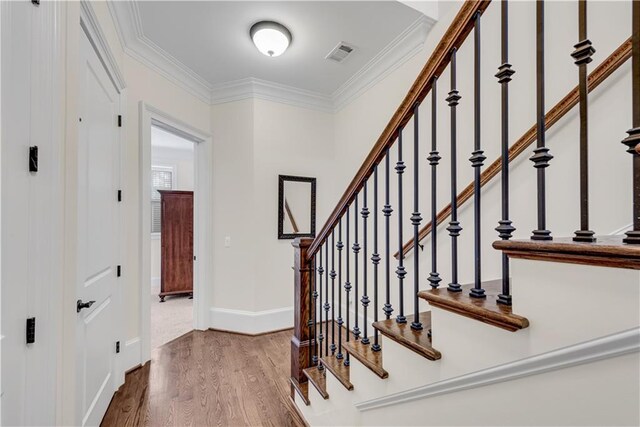 staircase with wood-type flooring and ornamental molding