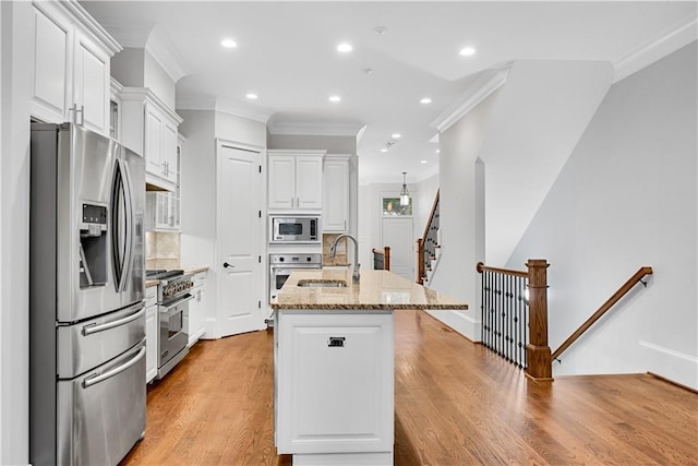 kitchen with white cabinets, a center island with sink, light wood-type flooring, stainless steel appliances, and light stone counters