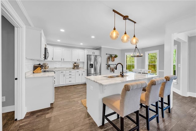 kitchen with sink, white cabinetry, decorative light fixtures, stainless steel appliances, and a kitchen island with sink