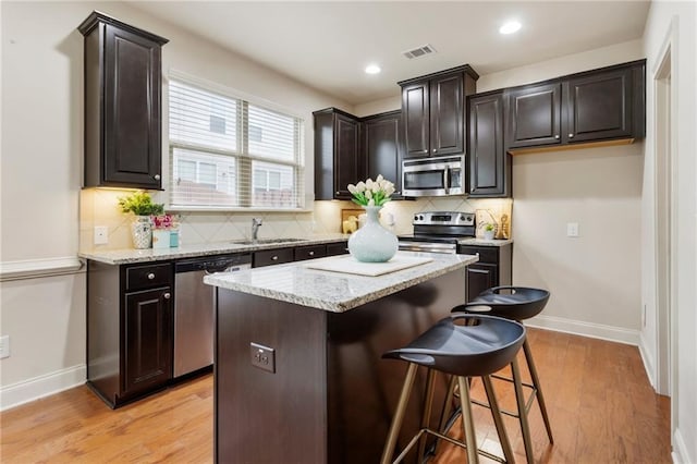 kitchen with appliances with stainless steel finishes, sink, light hardwood / wood-style floors, a kitchen island, and a breakfast bar area