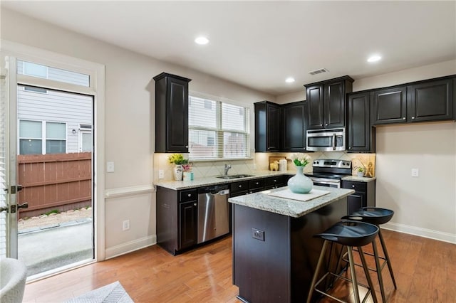 kitchen featuring sink, stainless steel appliances, a kitchen bar, a kitchen island, and light wood-type flooring