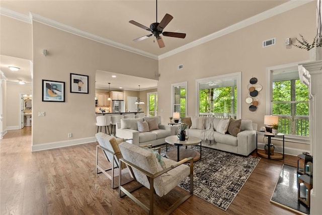 living room with light wood finished floors, a ceiling fan, a wealth of natural light, visible vents, and ornamental molding