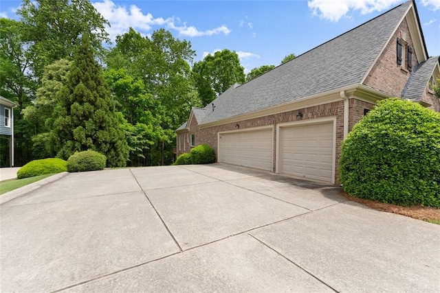 view of home's exterior featuring brick siding, driveway, a shingled roof, and a garage