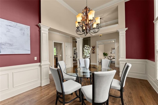 dining room featuring crown molding, wainscoting, wood finished floors, a chandelier, and ornate columns