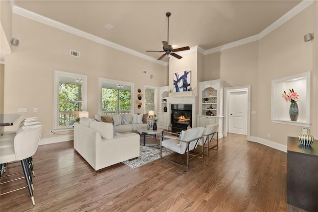 living room featuring a ceiling fan, a high ceiling, baseboards, and wood finished floors