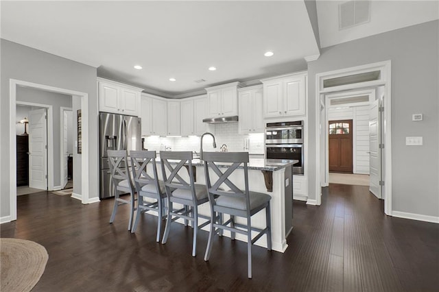 kitchen with a kitchen bar, white cabinetry, a center island with sink, and stainless steel appliances